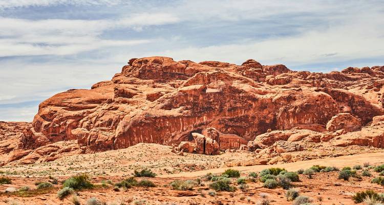 Paysage accidenté de grès rouge sous un ciel partiellement nuageux dans le désert.