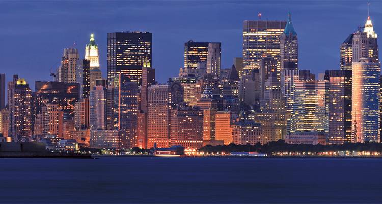 Nachtelijk panorama van New York City's verlichte wolkenkrabbers die reflecteren op de Hudson River.