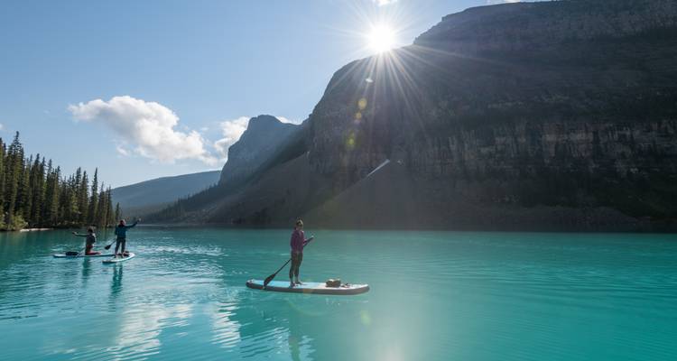 Les pratiquants de paddle glissent sur les eaux turquoise saisissantes d'un lac glaciaire sous les imposants sommets des montagnes Rocheuses et un soleil éclatant.