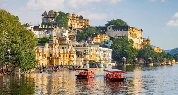 Boote voller Besucher fahren auf dem Pichola-See vor Udaipurs prunkvollem Stadtpalast.