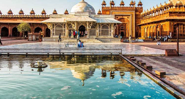 Reflektierender Teich und kunstvoller Marmorgrabstein im lebhaften Innenhof von Fatehpur Sikri.