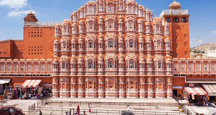 Ikonische rosa Sandsteinfassade von Jaipurs Hawa Mahal, die über einem belebten Straßenmarkt aufragt.