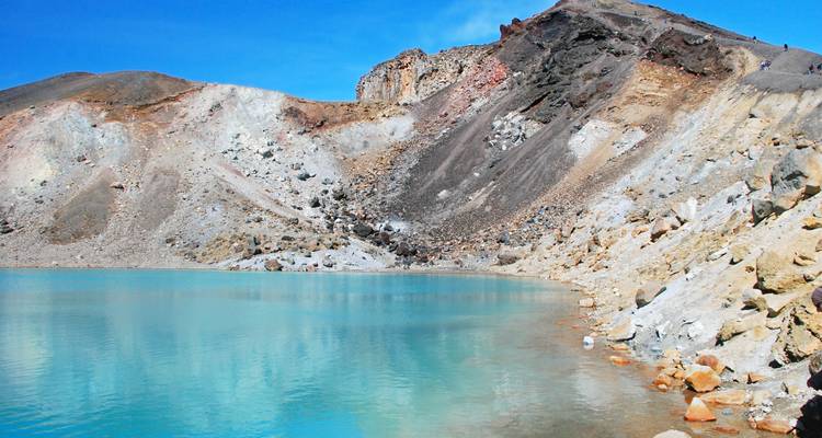 Türkisfarbener Alpensee, umgeben von hellen Klippen und Geröll unter einem strahlenden Himmel.