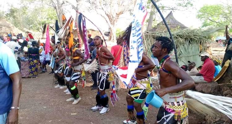Ligne de danseurs masculins en jupes traditionnelles tenant des bannières and des chasse-mouches en crin de cheval lors d'un festival en plein air.