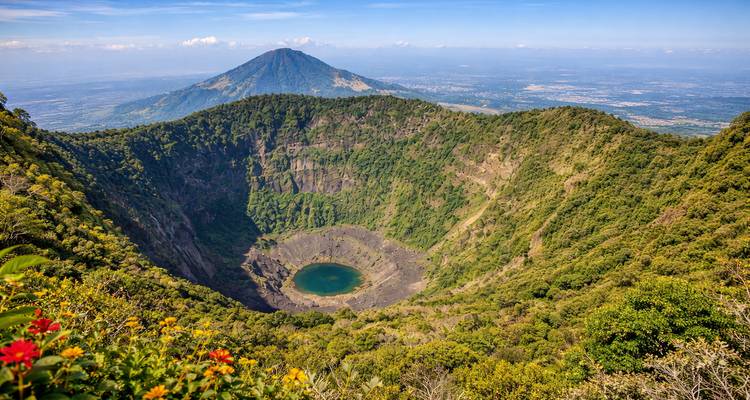 Cratère du volcan El Boquerón avec petite lagune verte au milieu de pentes luxuriantes et plaines panoramiques lointaines.