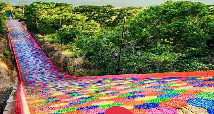 Long toboggan en plastique coloré serpentant en descente à travers la forêt verte dans un parc d'attractions.