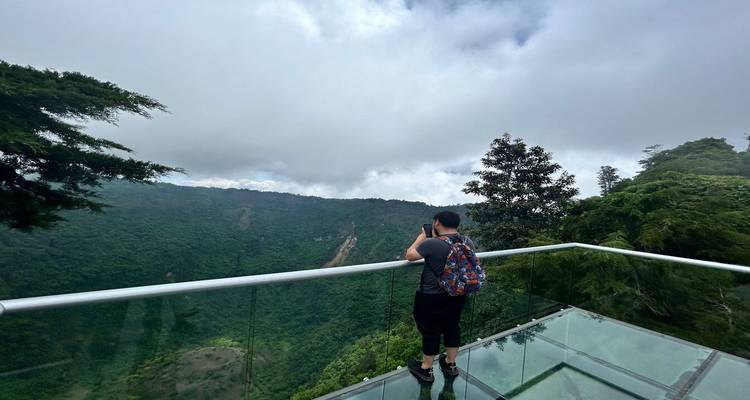 Visiteur debout sur une passerelle en verre surplombant les parois luxuriantes et verdoyantes du cratère sous un ciel nuageux dans le parc El Boquerón.