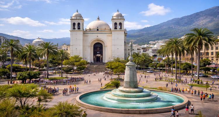 Place panoramique Gerardo Barrios avec la cathédrale de San Salvador, les palmiers et la fontaine centrale encadrée par les montagnes.