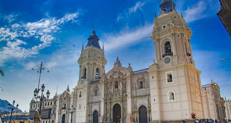 Grand Cathedral of Lima dominating Plaza Mayor under vivid blue sky with wispy clouds.