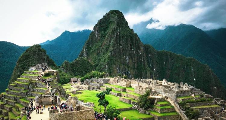 Iconic panoramic view of Machu Picchu ruins with Huayna Picchu peak rising behind lush green terraces and Andes mountains.