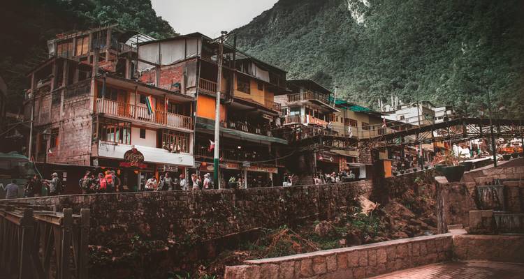 Bustling mountain town of Aguas Calientes with colorful buildings stacked along a river gorge beneath lush peaks.
