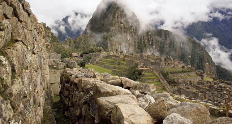 Misty morning view along stone walls of Machu Picchu overlooking terraces and dramatic peak shrouded in clouds.