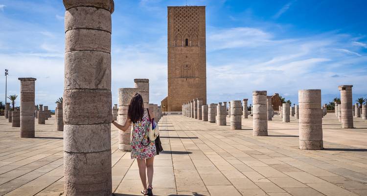 Toeriste vrouw staat tussen stenen zuilen van de Hassan Toren locatie in Rabat, kijkend naar de hoge bakstenen minaret.
