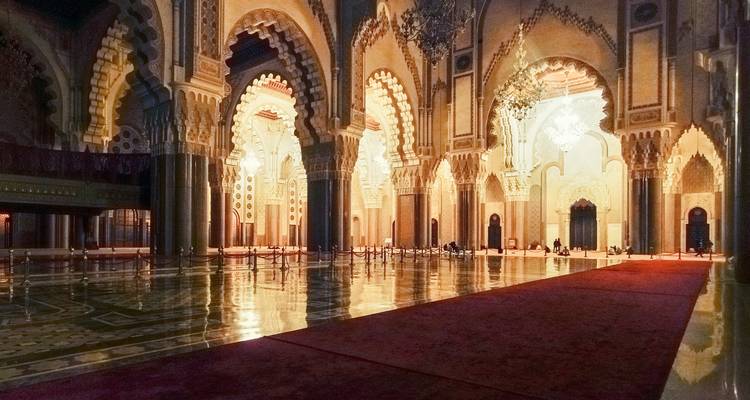 Zwak verlichte, sierlijke interieurhal van de Hassan II-moskee met glimmende marmeren vloer, kroonluchters en gesneden bogen.