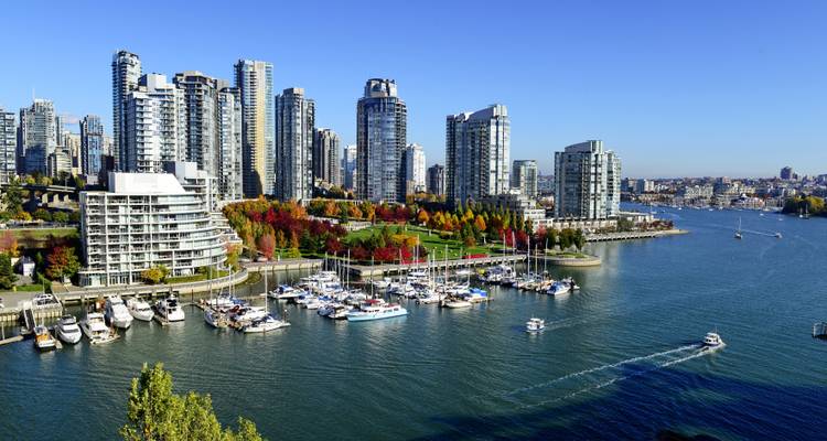Moderne skyline van Vancouver met hoge glazen torens die uitkijken over een jachthaven vol zeilboten op een heldere zonnige dag.