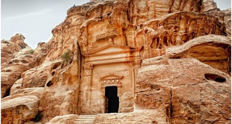 Façade de tombeau taillée dans la roche avec colonnes classiques et fronton triangulaire intégrée dans les falaises de grès rose-rouge de Pétra.