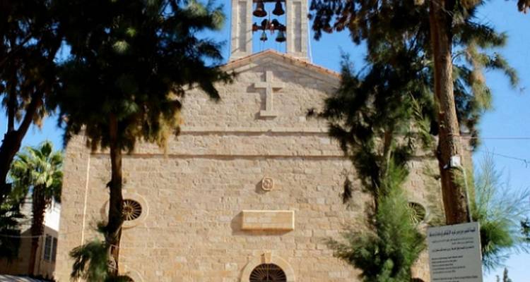 Façade d'église en pierre avec clocher et croix encadrée par de grands pins