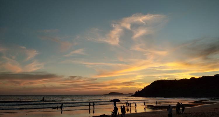 Coucher de soleil sur une plage de Goa avec des nuages pastel, des vagues douces et des visiteurs en silhouette le long du rivage