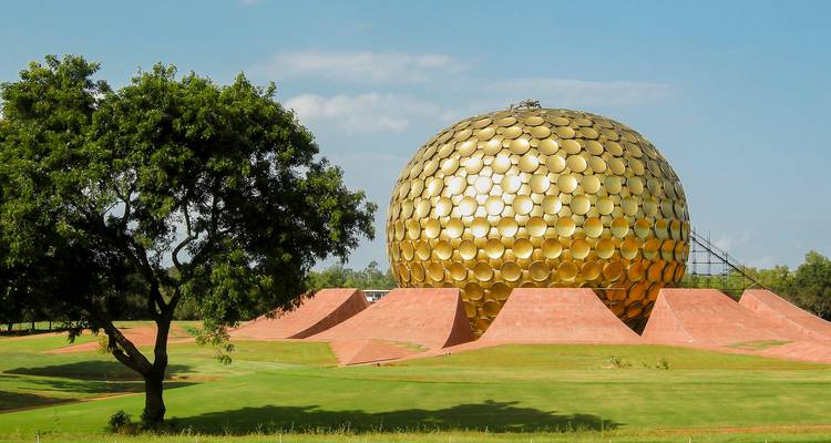 Gouden bol van Matrimandir die glimt te midden van groene gazons en blauwe lucht in Auroville