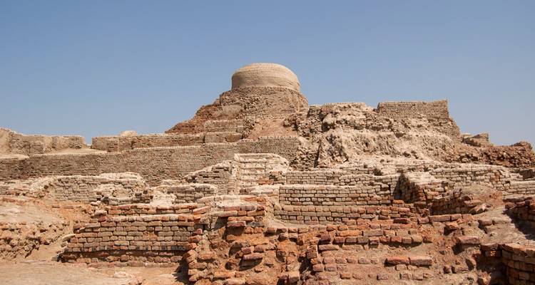 Alte Ziegelruinen und eine kuppelförmige Stupa an der archäologischen Stätte von Mohenjo-Daro unter klarem Himmel.
