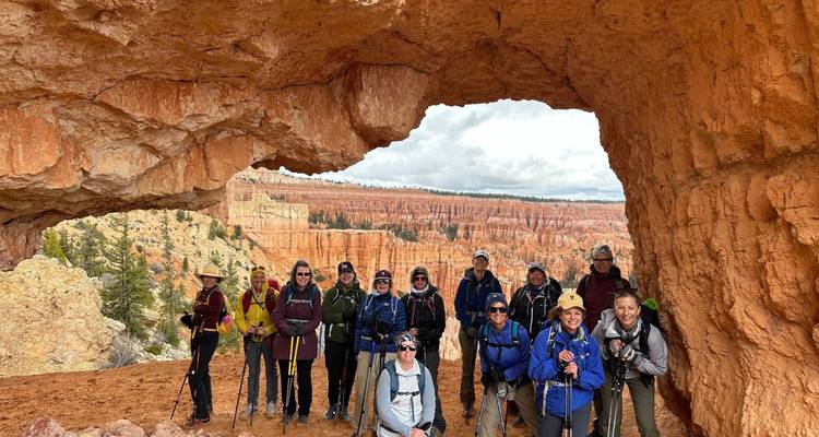 Große Wandergruppe posiert unter einem natürlichen Bogenfenster mit Blick auf Bryce Canyons Hoodoos und orangefarbene Klippen.