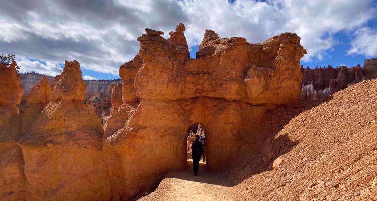 Einzelner Wanderer geht durch natürlichen Sandsteintunnel inmitten zerklüfteter Hoodoos und orangefarbenem Sand im Bryce Canyon.