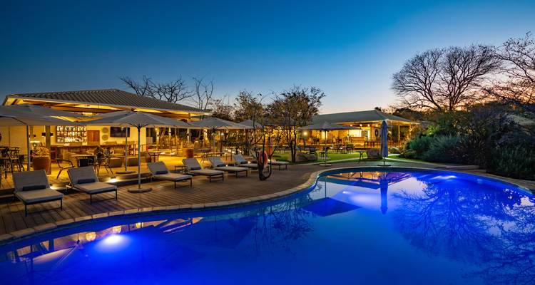 A stylish lodge with poolside loungers illuminated at twilight beneath a deep blue sky