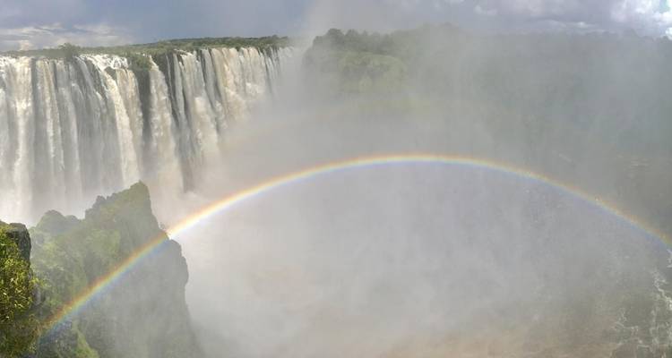 Spectacular view of Victoria Falls with mist and a full rainbow arching over the gorge