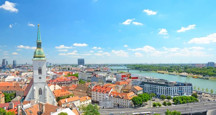 Helles Panorama von Bratislava mit dem Turm der St.-Martins-Kathedrale und der Donau unter klarem Himmel.