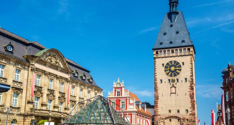 Historischer Uhrenturm und reich verzierte Fassaden in Speyer unter einem strahlend blauen Himmel.