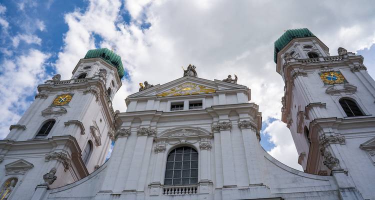 Vue en contre-plongée des tours baroques blanches de la cathédrale de Passau couronnées de dômes verts sur un ciel nuageux.