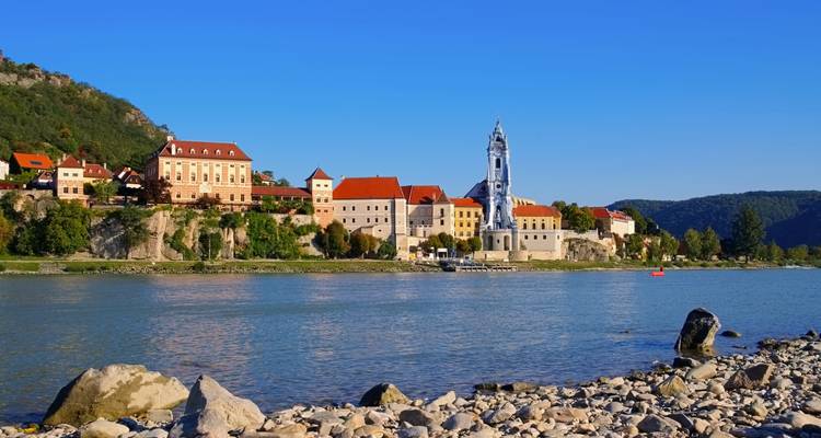 Village pittoresque de Dürnstein au bord du fleuve avec son clocher bleu encadré par des collines boisées.