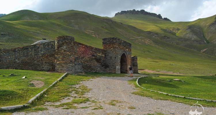 Stenen karavanserai genesteld in weelderige groene vallei met dramatische heuvels die erachter oprijzen