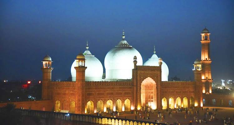 Mezquita Badshahi iluminada al anochecer con cúpulas que brillan blancas contra un cielo azul profundo