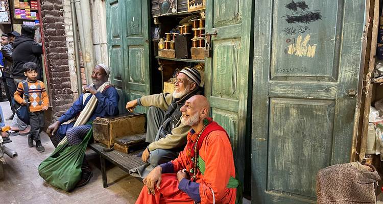 Hombres ancianos en atuendo tradicional se relajan afuera de un viejo taller en el bazar de Lahore.