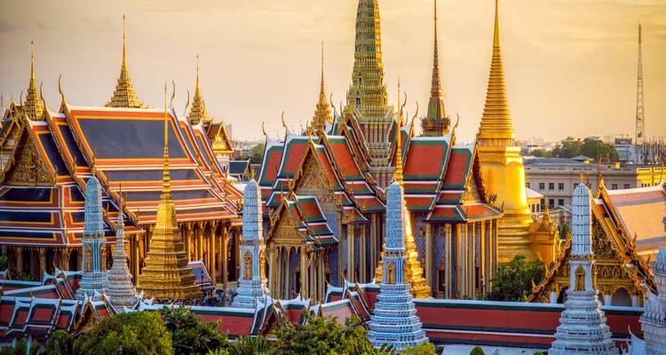 Lumière dorée illuminant les flèches ornées et les toits colorés du complexe du Grand Palais de Bangkok