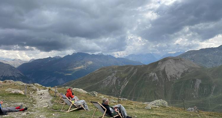 Des voyageurs se reposant sur des chaises longues au sommet d'une crête avec des nuages orageux spectaculaires au-dessus des pics alpins.