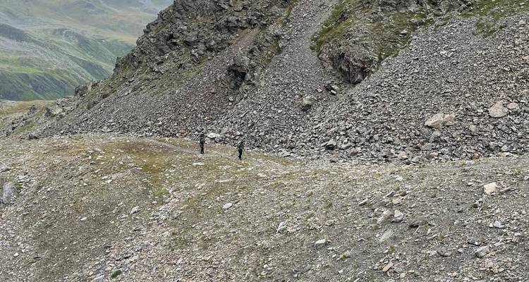 De minuscules randonneurs traversent une pente d'éboulis aride entourée de parois rocheuses escarpées.
