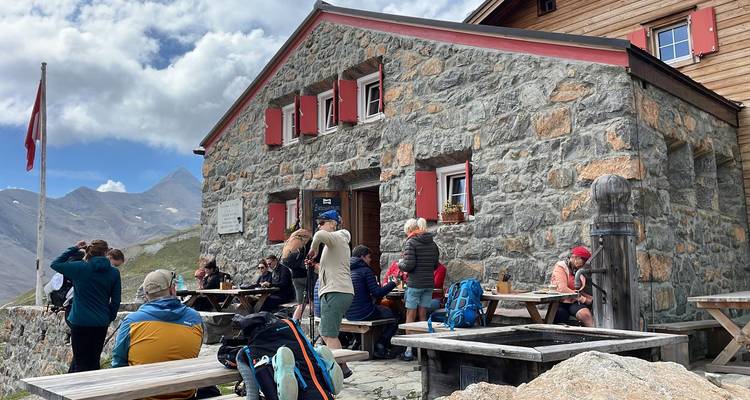 Grand groupe de randonneurs socialisant devant un refuge de montagne en pierre avec drapeau suisse.