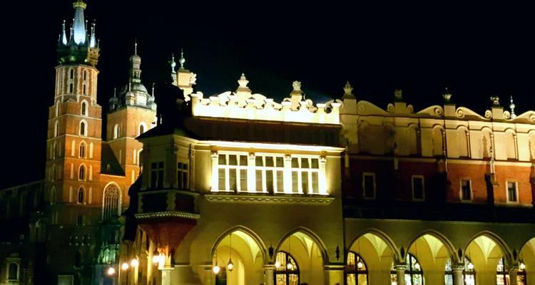 Torres góticas iluminadas y arcadas renacentistas de la plaza de Cracovia contra un cielo negro