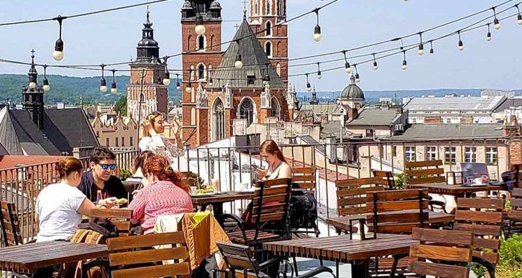 Café en la azotea con luces de hilo y amigos cenando mientras contemplan la basílica de Cracovia
