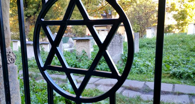Puerta de hierro forjado con Estrella de David que da vista a un antiguo cementerio judío cubierto de vegetación