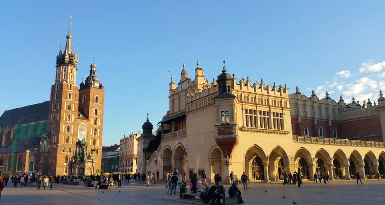 Hora dorada en la concurrida Plaza del Mercado Principal de Cracovia con las arcadas de los puestos de tela y la basílica bañadas en luz cálida