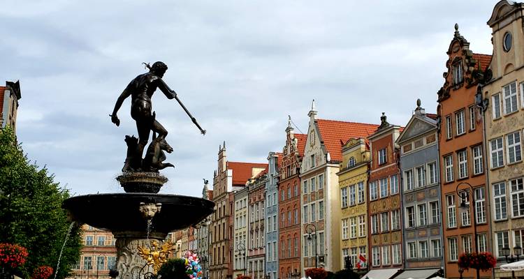 Silueta de la Fuente de Neptuno ante casas de hastiales coloridos en el Mercado Largo de Gdansk bajo cielos nublados.
