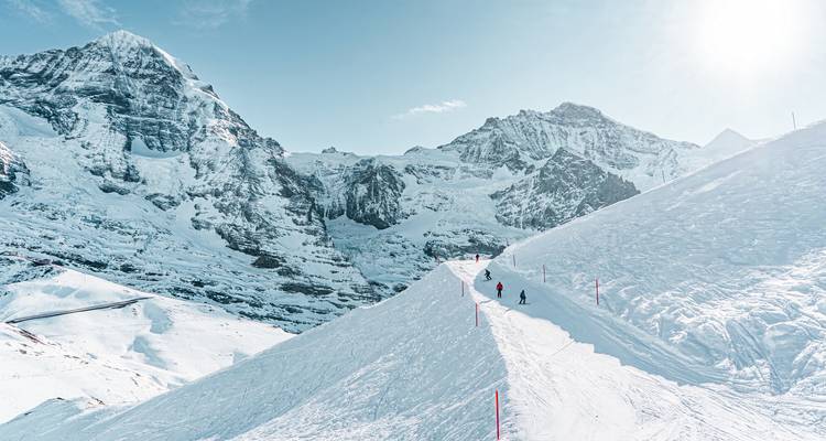 Les skieurs progressent le long d'une crête ensoleillée au milieu d'un vaste panorama de montagnes escarpées couvertes de neige.