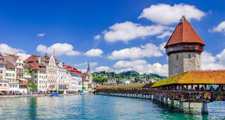 Scène estivale lumineuse du pont de la Chapelle enjambant la rivière Reuss turquoise avec les façades colorées de la vieille ville et des nuages duveteux.