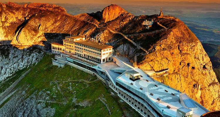 La lumière dorée du soleil baigne l'hôtel du sommet et les falaises calcaires escarpées du mont Pilate au crépuscule.