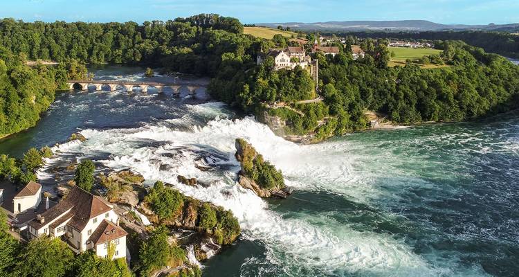 Vue aérienne panoramique des chutes du Rhin avec des eaux blanches tumultueuses et la campagne verdoyante environnante.