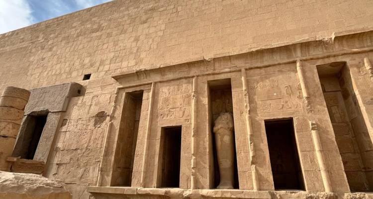 Fachada de un templo funerario del antiguo Egipto con relieves tallados y puertas altas bajo un cielo brillante.