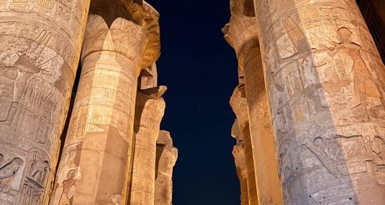 Las columnas cubiertas de jeroglíficos iluminadas de un templo egipcio brillan cálidamente contra el cielo nocturno.
